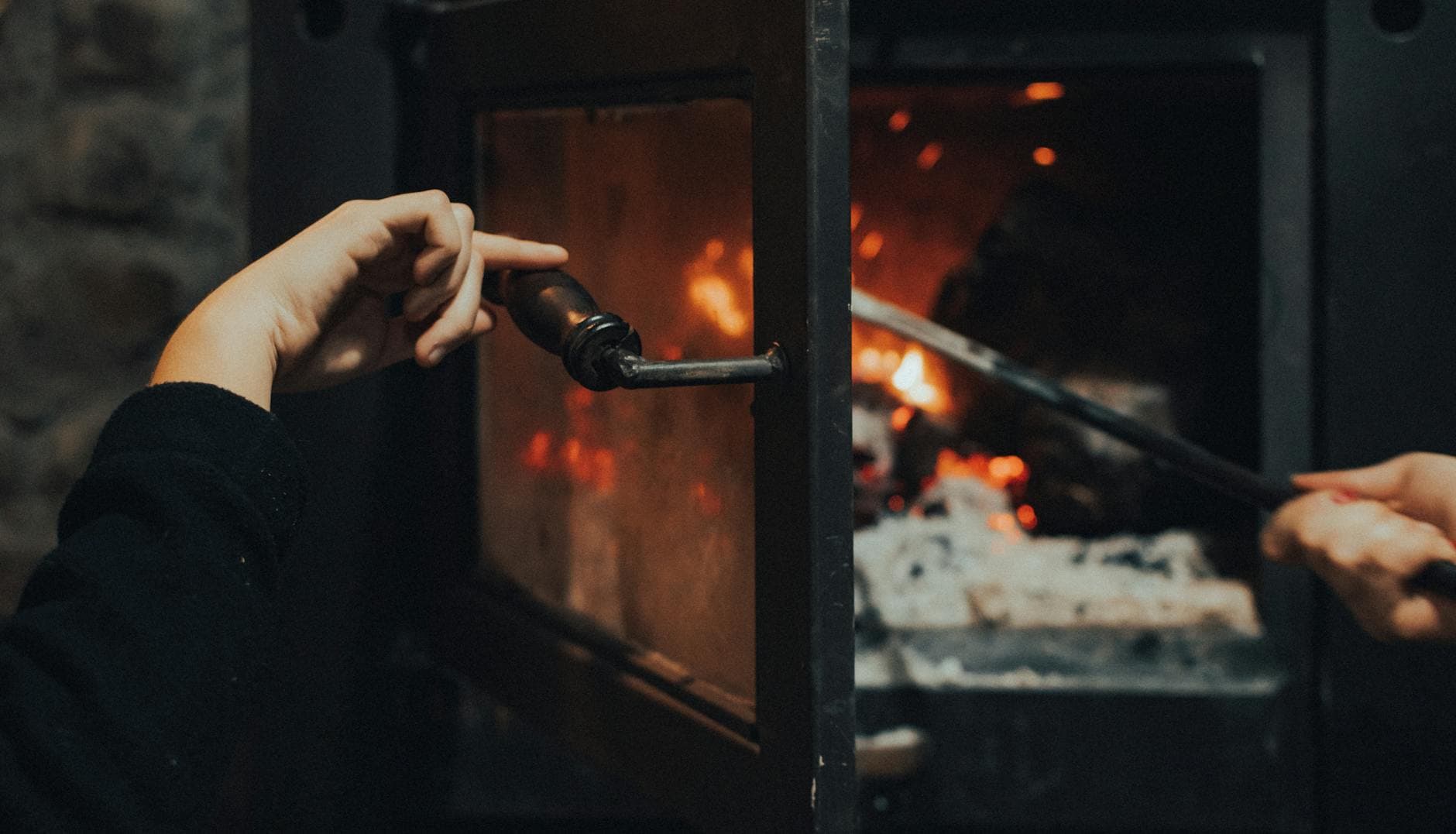 Close-up of hands tending a warm indoor fire, offering a cozy atmosphere.