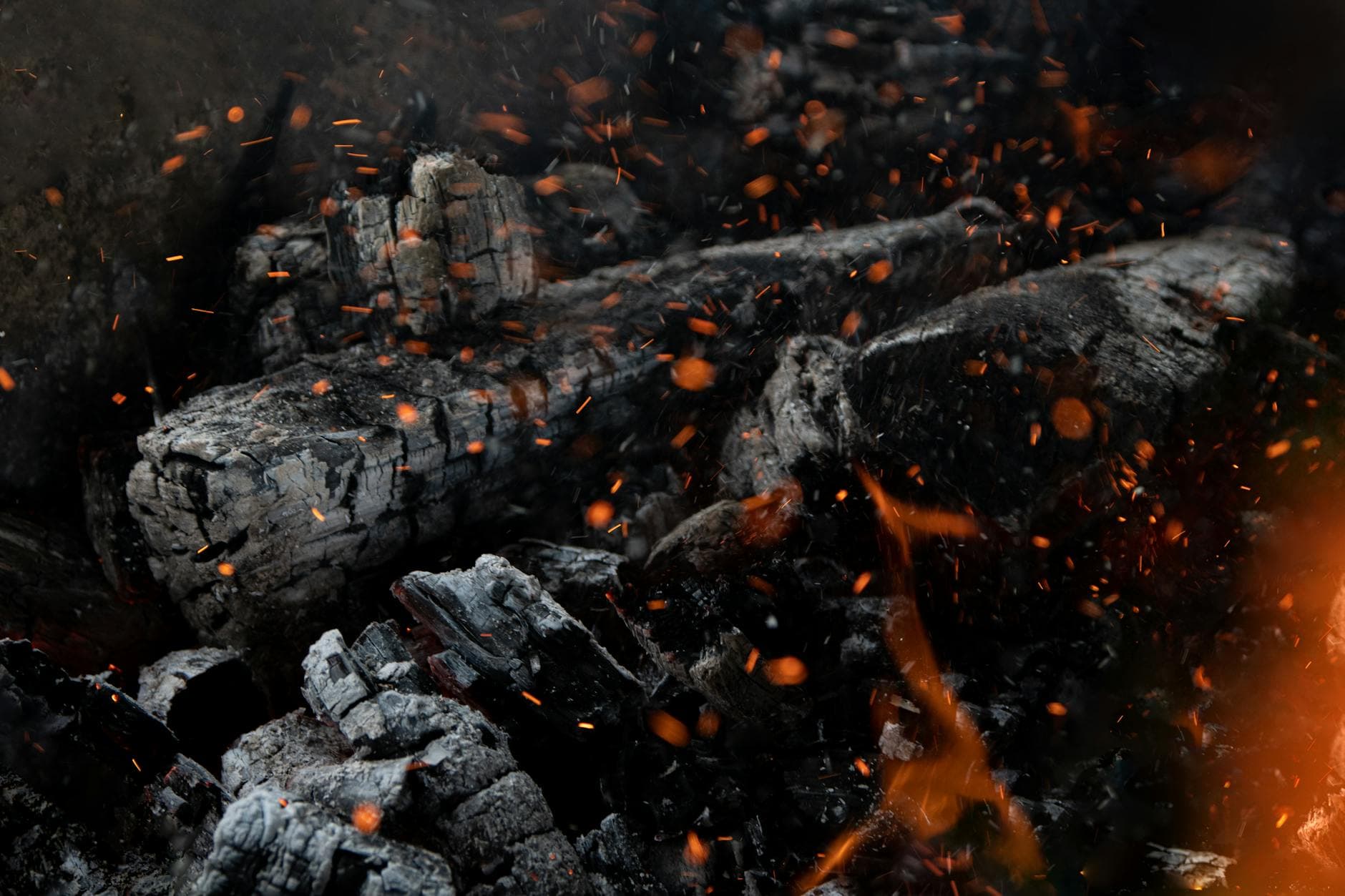 Dramatic close-up of glowing embers and partially burnt charcoal with sparks.